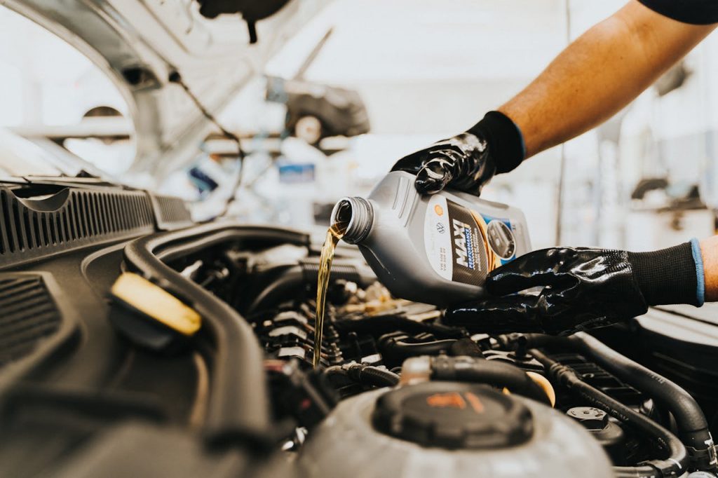pexels photo 13065690 Close-up of a mechanic pouring engine oil into a car engine in an auto repair shop.