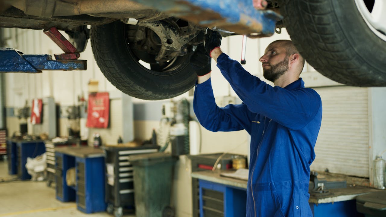 Mechanic in blue overalls inspecting vehicle undercarriage in a professional workshop.